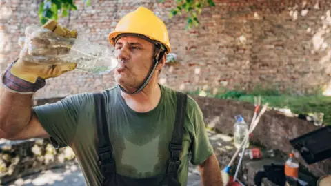 Getty Images Construction worker who is very hot and drinking water