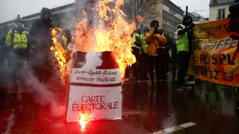 Reuters Protesters wearing yellow vests stand near a burning facsimile voter registration card during a demonstration by the "yellow vests" movement in Nantes, France, 15 December.