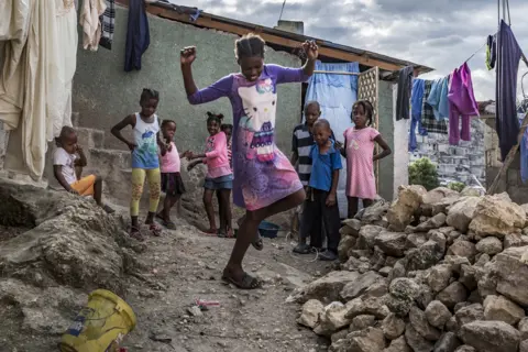 Tariq Zaidi A young girl plays hopscotch in front of her house while her friends and neighbours look on