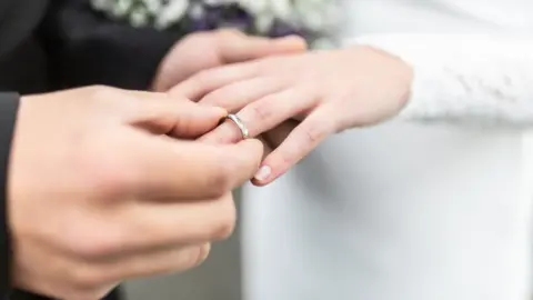 Getty Images A groom puts a wedding ring on a bride's finger