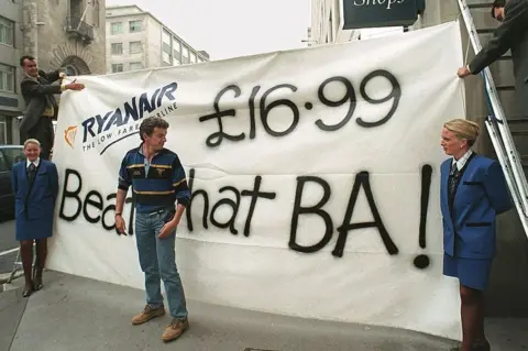 AFP Ryanair's chief executive Michael O'Leary looks at a banner the company erected outside of rival British Airways travel shop 03 September. 1998