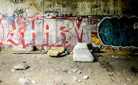 BBC A bed sits empty on the side of the tracks, surrounded by used needles