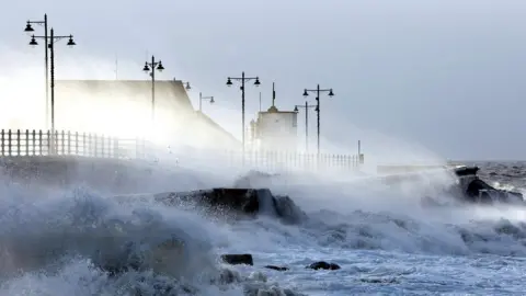 PA Waves breaking over sea wall with houses behind