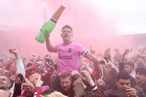 PA Media Northampton Town fans and Sam Hoskins celebrate promotion after the Sky Bet League Two match at Prenton Park