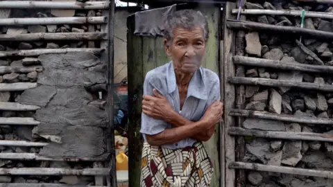 Getty Images A shivering woman stands outside her damaged home