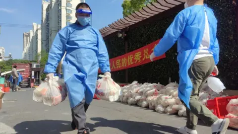 Getty Images A volunteer carries daily necessities for residents at a residential community in Songjiang district amid the COVID-19 resurgence on April 17, 2022 in Shanghai,