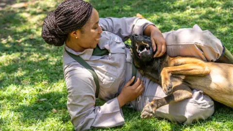 Paul Joynson-Hicks A trainee dog handler lounging on the grass and playing with a dog in Arusha, Tanzania