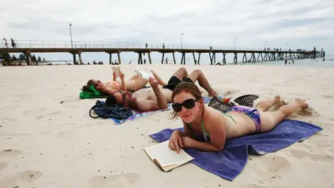 Getty Images Two women and a man lying on the beach at Glenelg in South Australia.