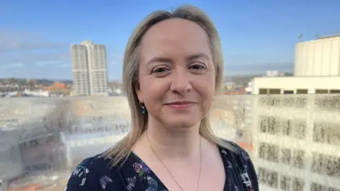 BBC Louise Sheppard smiling with tall buildings behind her