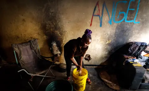 BBC/SHIRAAZ MOHAMED Angela doing her daily chores, washing clothing from a plastic bucket in the derelict San Jose building in Johannesburg, South Africa