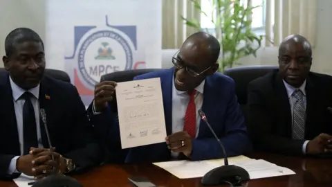 Reuters Haiti's Minister of Planning and External Cooperation Aviol Fleurant (centre) shows a statement about the Oxfam case at a news conference in Port-au-Prince on 13 June 2018