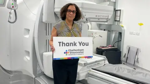 Gloucester Hospitals Charity Dr Janelle Reyes-Goddard standing in front of the scanner with a thank you sign