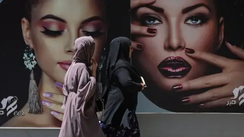 AFP Burqa clad women walk past a billboard put up on the wall of a beauty salon in Kabul on August 7, 2021