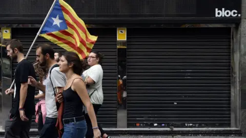 AFP This file photo taken on 3 October 2017 shows people walking past a closed store during a general strike in Catalonia called by Catalan unions in Barcelona