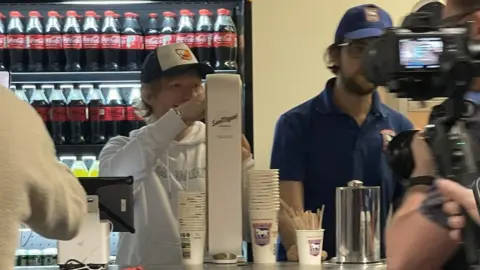 Daisy Hendry Ed Sheeran serving customers behind the bar at Ipswich Town football club