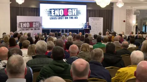 The meeting showing a sign saying 'enough lives lost on the the A5'