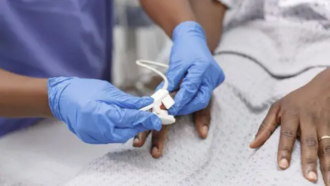 Getty Images Medic places a pulse oximeter on the finger of a black hospitalized patient