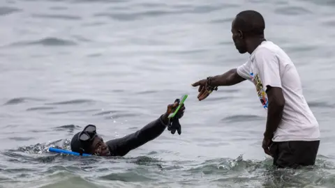 Jerome Favre/EPA-EFE/REX/Shutterstock An ocean diver hands over a phone to another man on 24 July 2023