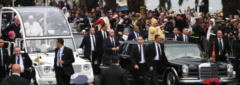 AFP/Getty Images King Mohammed VI (R) waves to the crowd from his car as he arrives with Pope Francis (L) the pontiff's arrival