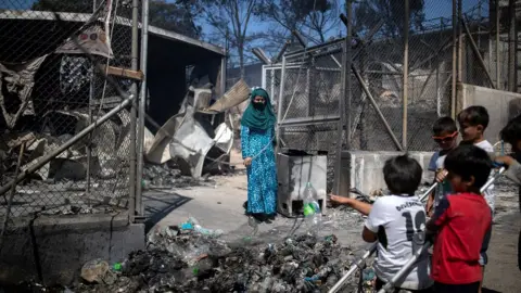 Reuters A woman stands next to destroyed shelters following a fire at the Moria camp for refugees and migrants on the island of Lesbos, Greece, 9 September 2020