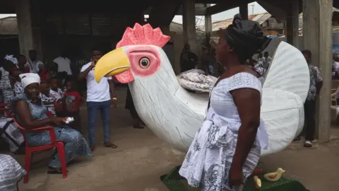 Getty Images A woman touching a coffin that is shaped like a rooster