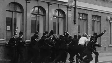 Getty Images A group of police officers run with their batons raised