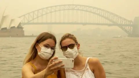 Getty Images Two German tourists pose for a selfie, wearing breathing masks, as heavy smoke blankets Sydney skyline