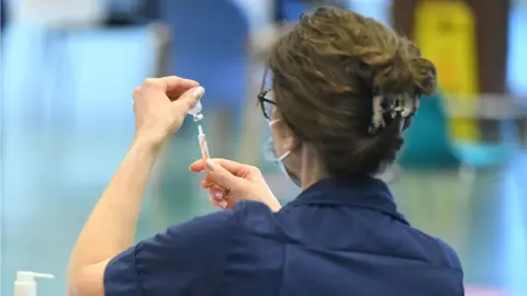 Dominic Lipinski/PA A woman holding up a vaccine vial
