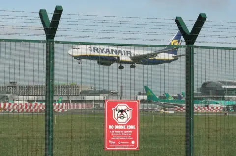 PA A plane flying into Dublin Airport behind a fence with a sign that reads: No drone zone