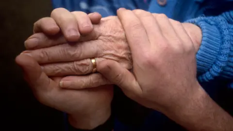 BBC Carer holding the hand of an elderly lady
