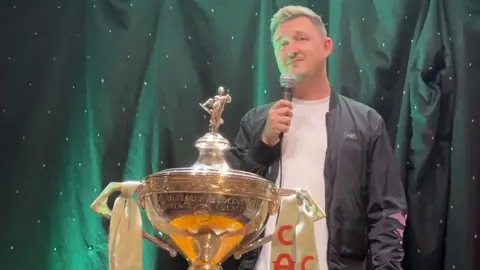 Kyren Wilson standing next to his trophy.