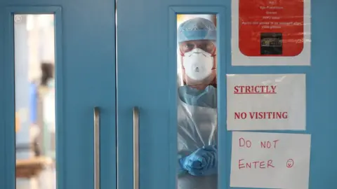 PA Media A medical professional looks through a window in a door of Covid-19 recovery ward at Craigavon Area Hospital