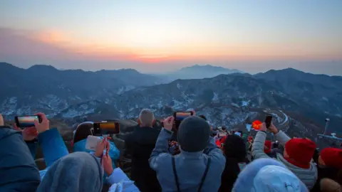 VCG Tourists on the Great Wall take photos of the sunrise with their phone cameras