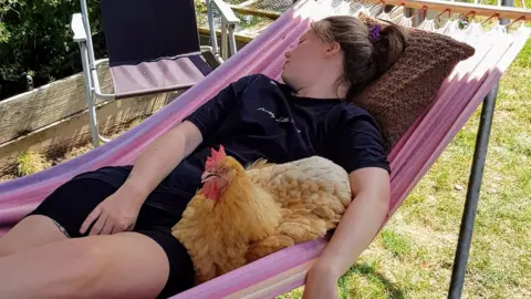 Sarah Chidwick A young woman asleep in a hammock with her pet chicken