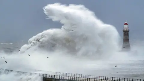 PA Media Waves crash against the sea wall and Roker Lighthouse in Sunderland