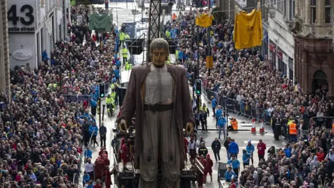 PA Hundreds watch "Giants" street puppet, The Giant Man, during a street theatre performance in Liverpool