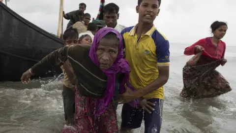 Getty Images A young Rohingya man carries an elderly woman, after the wooden boat they were travelling on from Myanmar crashed into the shore and tipped everyone out in Dakhinpara, Bangladesh