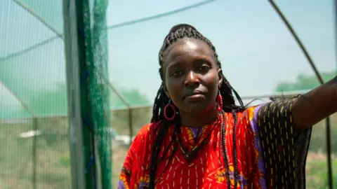 Mumbi Bakari/ActionAid Women stands in greenhouse with her arm resting