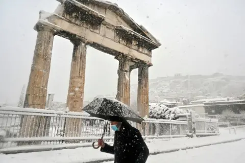 AFP A man holding an umbrella in snow near the Roman Agora in central Athens