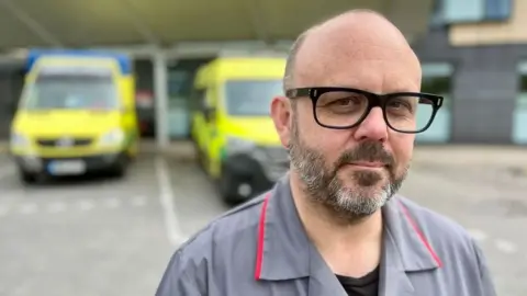 Matt Precey/BBC Nurse in front of two ambulances