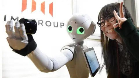 Getty Images A woman poses as humanoid robot Pepper takes a picture at a booth of digital marketing company IMJ Corporation during the Pepper App Challenge 2015 in Tokyo on February 22, 2015. Mobile phone carrier Softbank, which developed the humanoid robot, held the application competition for Pepper on February 22.