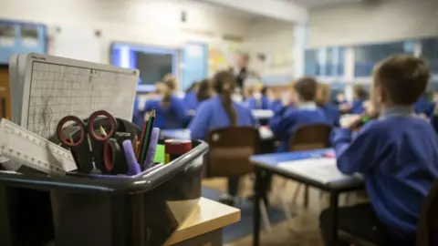 PA Media File image of a box of stationery, in front of out of focus pupils in a classroom