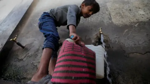 Reuters A boy fills canisters with water at a public tap in Sanaa, Yemen (13 October 2017)