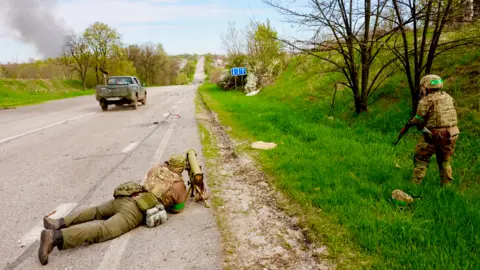 Darren Conway / BBC With Ukrainian troops by a roadside to the north of Kharkiv, smoke visible in the distance