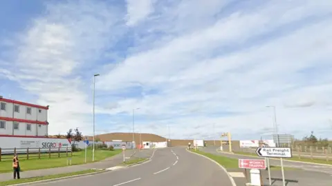 Google Entrance to rail freight terminal, showing road signs and temporary site buildings