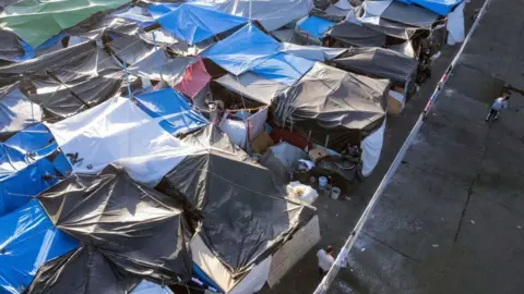 Getty Images Aerial view of an improvised camp of asylum seekers at El Chaparral border crossing near the Mexico-United States border in Tijuana, Baja California state, Mexico, on November 8, 2021