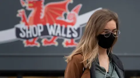 Getty Images Woman in face mask with dragon on shop behind her in Cardiff