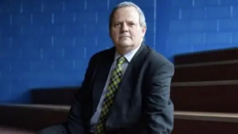 John Kendall John Kendall sitting in a school auditorium