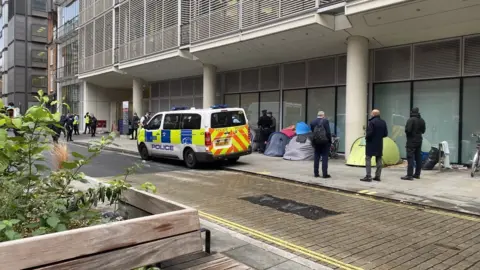 Mariam Issimdar/BBC Image showing a police van parked on the street, with multiple officers present