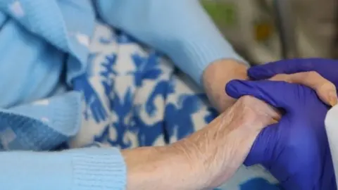 PA Media Elderly woman holding hands with carer wearing gloves